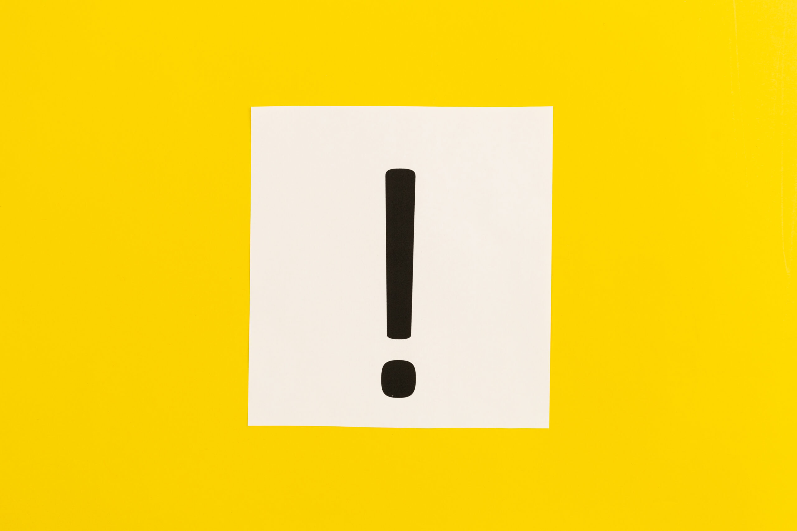 Exclamation mark on white paper on yellow background, flat lay.